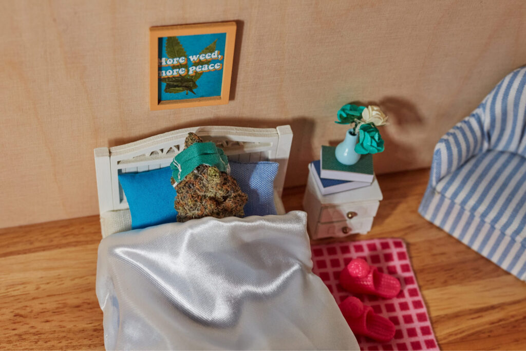 A cannabis nug lying in bed with a sleeping mask referencing a nighttime cannabis strain.